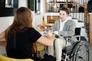 A woman in a wheel chair doing business with another woman who is looking at her phone