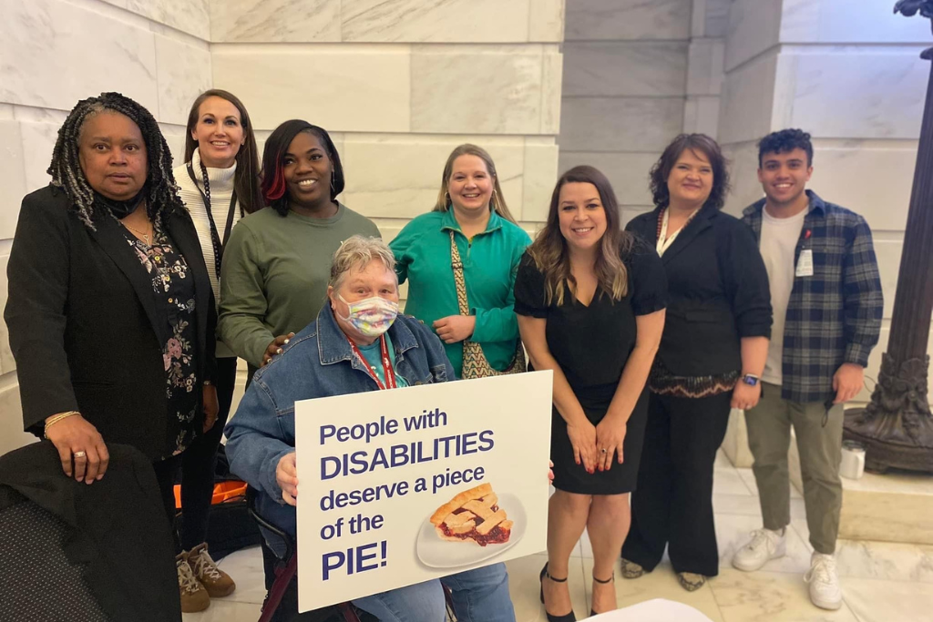 A group of individuals gathered in the Capitol holding a sign that reads "People with disabilities deserve a piece of the pie."