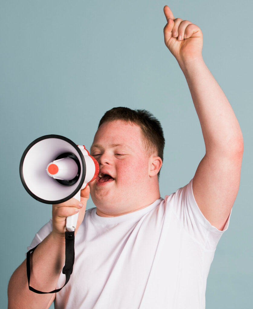 Man with down syndrome holding megaphone in one hand and raising his other hand in the air.